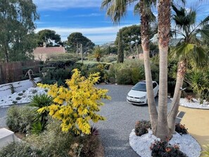 A residential driveway with a white car parked, surrounded by various plants and trees. - Superb T2 RDJ in quiet Sanary (Sanary-sur-Mer)