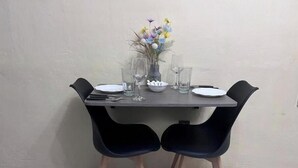 Una mesa de comedor con dos sillas negras, un jarrón con flores y un cuenco de cubiertos.