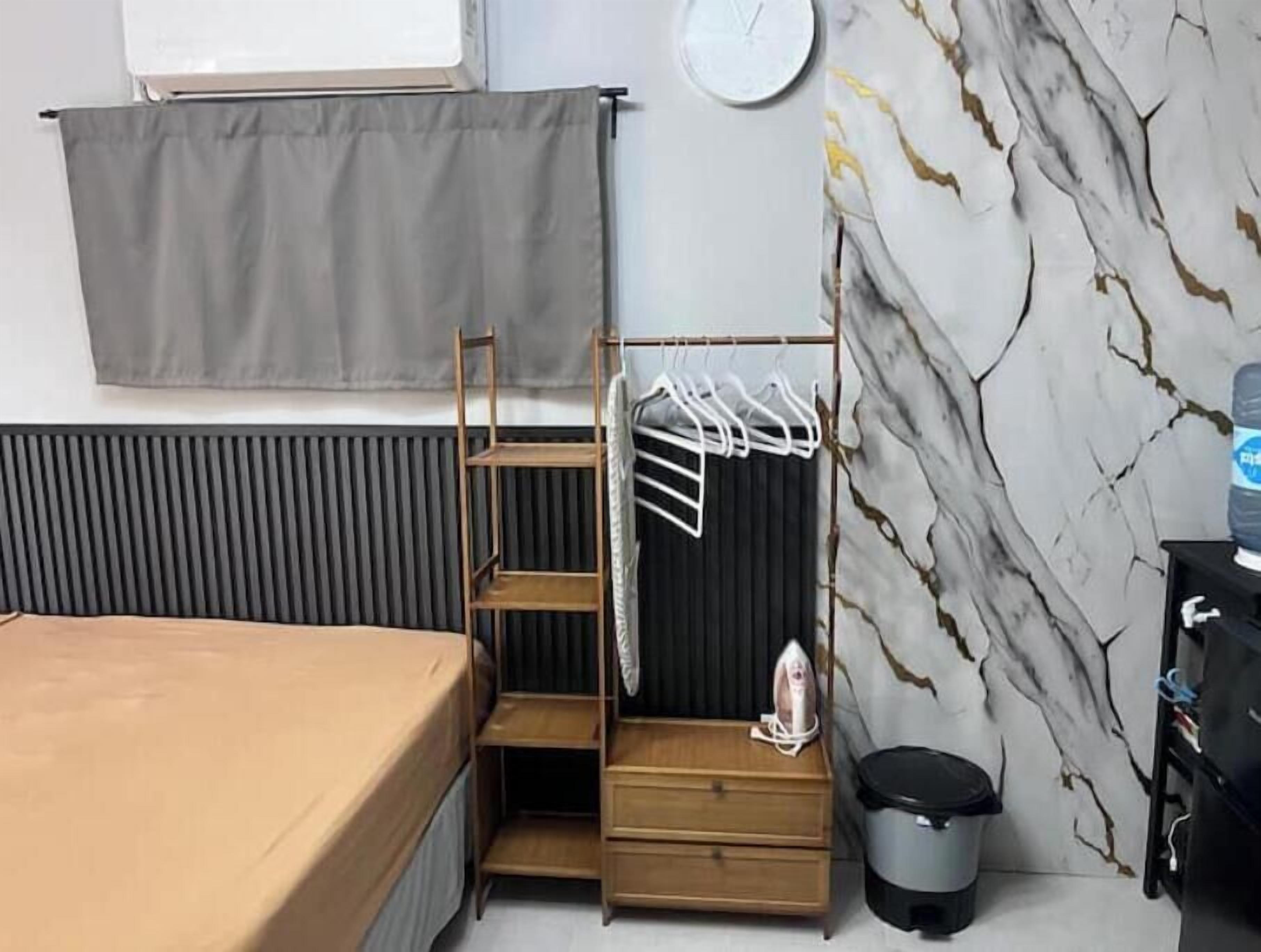 Un dormitorio con cama, una estantería de madera con ropa colgada, un radiador, un reloj y una pared con diseño de mármol.