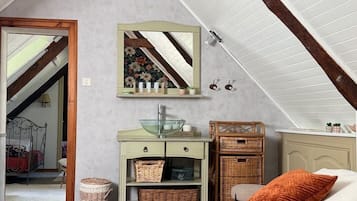 A bedroom with a sloped ceiling, a bed with a patterned bedspread, a dresser with baskets, a mirror, and a wicker chair.