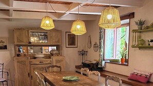 Un coin repas rustique avec une table et des chaises en bois, un luminaire suspendu et une fenêtre donnant sur un paysage verdoyant.