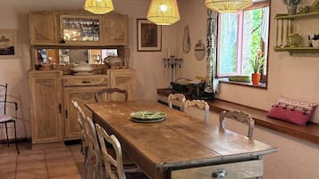 A rustic dining area with a wooden table and chairs, a hanging light fixture, and a window with a view of greenery.