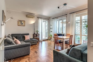 A spacious living area with a grey sofa, a dining table with chairs, and large windows with curtains. - Zima’s House Elegant Penthouse in Central Rome (Roma)