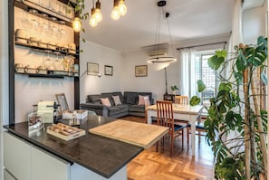 A modern kitchen with a central island, a dining area with a table and chairs, a gray sofa, and a large window with natural light. - Zima’s House Elegant Penthouse in Central Rome (Roma)