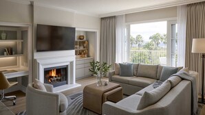 Una sala de estar moderna con chimenea, un conjunto de sofá, un televisor de pantalla plana y vistas a palmeras.
