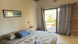 Ein Schlafzimmer mit einem Bett, einem gerahmten Bild an der Wand, einem Deckenventilator und Blick durch ein Fenster.