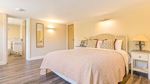 A bedroom with a large bed, a nightstand with a lamp, a mirror, and a door leading to a bathroom. - Chestnut Cottage in Bix (Bix)