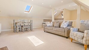 A spacious loft-style living area with a high ceiling, a dining table with chairs, a sofa, and a patterned rug. - Chestnut Cottage in Bix (Bix)