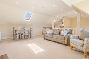 A spacious loft-style living area with a high ceiling, a dining table with chairs, a sofa, and a patterned rug. - Chestnut Cottage in Bix (Bix)
