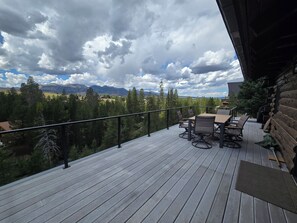 A wooden deck with a table and chairs, overlooking a forest and mountains. - Cabin by the Creek in Stanley Basin (Sawtooth City)