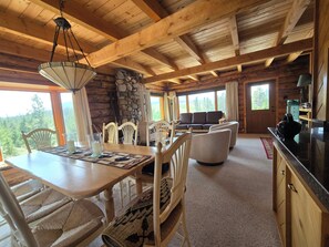 A wooden cabin interior with a dining table, chairs, a sofa, and a kitchen area.