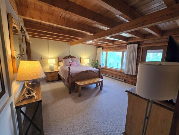 A wooden cabin bedroom with a bed, bedside lamps, a bench, and a large window.