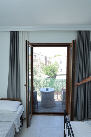 Habitación con cama, una silla, una mesa y vista a través de una puerta de cristal de un área exterior con una mesa redonda y sillas.