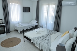 A hotel room with two beds, a TV, an air conditioner, and a desk with a kettle. - Adena Pansiyon (Küçükköy)