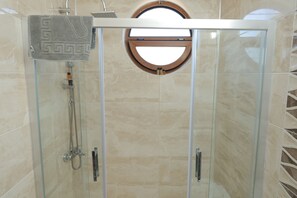 A glass-enclosed shower with a towel rack, a circular window, and a showerhead. - Adena Pansiyon (Küçükköy)