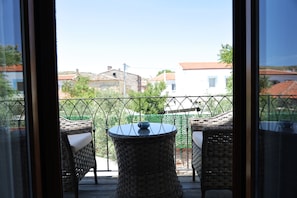 A balcony with wicker furniture and a table, overlooking a residential area with houses and greenery. - Adena Pansiyon (Küçükköy)