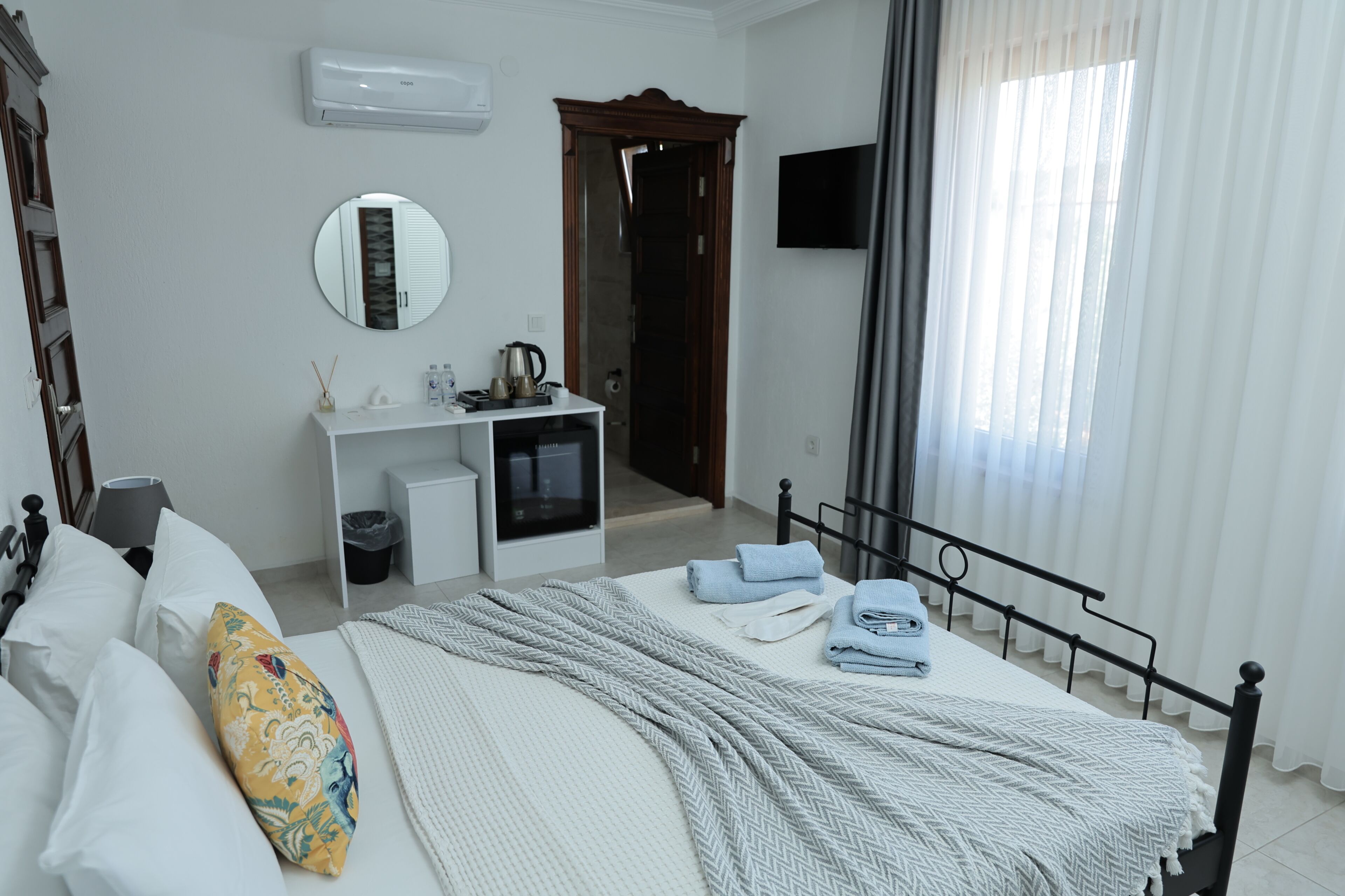 Un dormitorio con cama, mesita de noche, espejo y televisor montado en la pared.