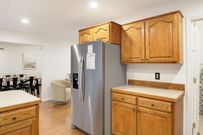 Une cuisine de taille réduite, avec des meubles en bois, un réfrigérateur en acier inoxydable et une chaise de couleur beige.