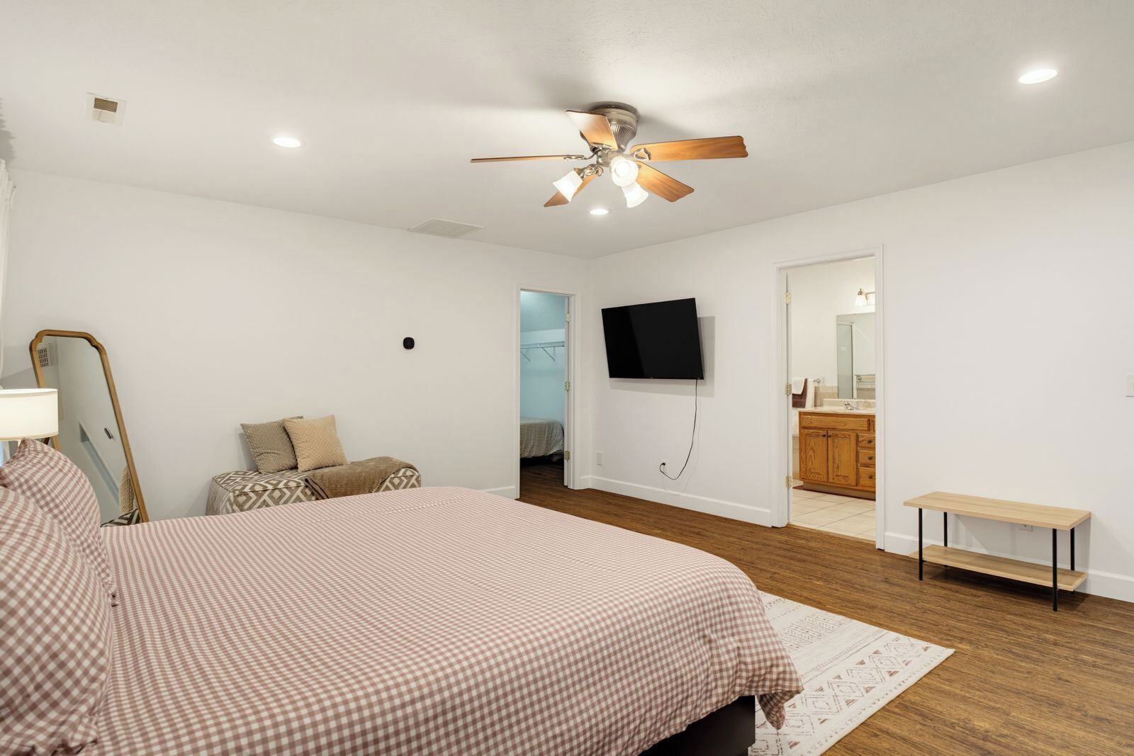 Un dormitorio con una cama grande, un ventilador de techo, un televisor y un baño visible a través de una puerta abierta.