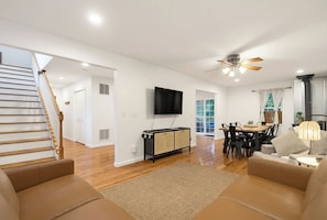 A spacious living area with a staircase, a flat-screen TV, a dining table with chairs, and a ceiling fan. - wildflower retreat (McGaheysville)