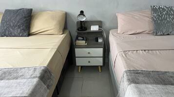 Un dormitorio con dos camas, una mesita de noche con lámpara, libros y una regleta eléctrica.