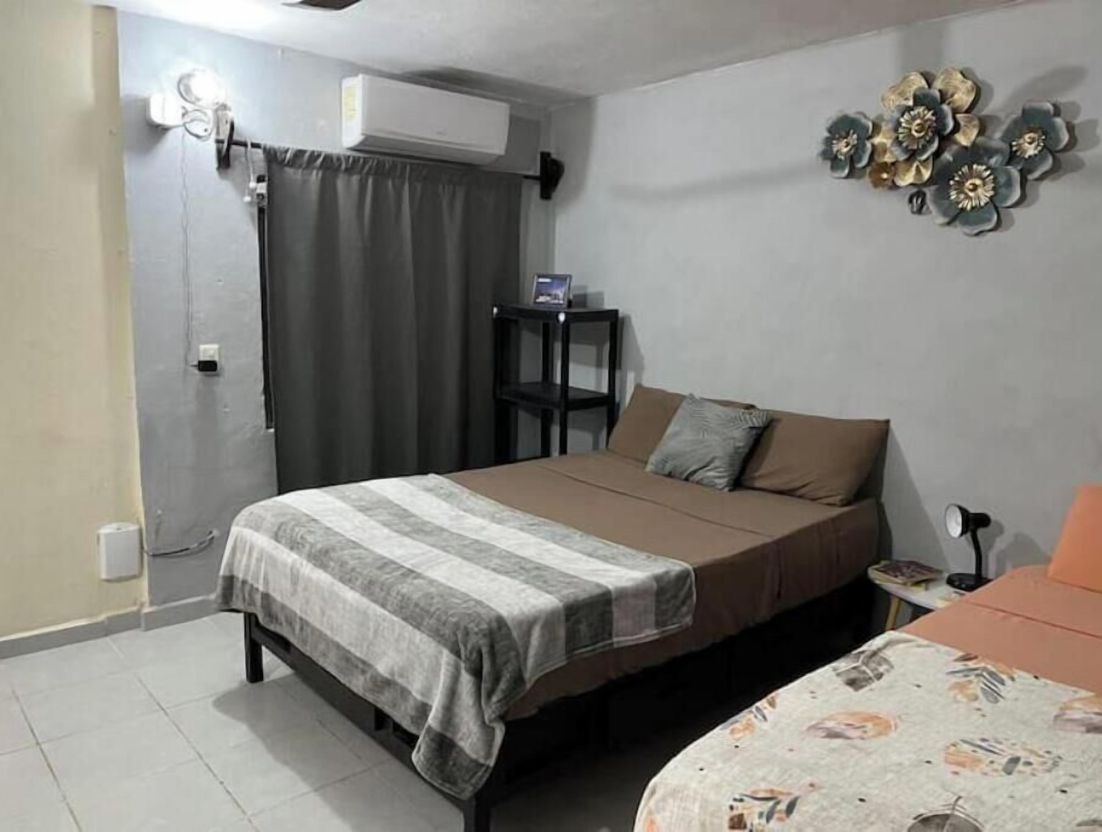 Un dormitorio con cama, mesita de noche, una pequeña mesa con lámpara y aire acondicionado instalado en la pared.