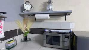 A kitchen with a microwave, a shelf with a clock and a vase, a roll of paper towels, and a plant. - Apartment with Wi-Fi, A/C, and parking—near downtown and the boulevard (Chetumal)