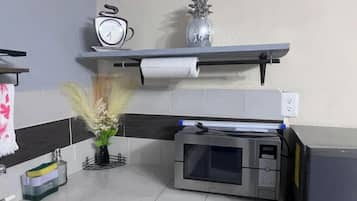 A kitchen with a microwave, a shelf with a clock and a vase, a roll of paper towels, and a plant.