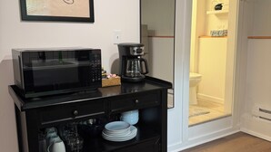 Een kitchenette met een magnetron, koffiezetapparaat en opslagplanken.