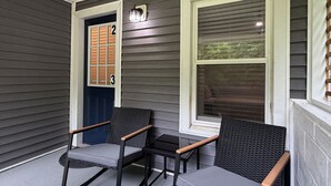 Een veranda met twee stoelen en een tafel, een deur met een nummer en een raam met luiken.