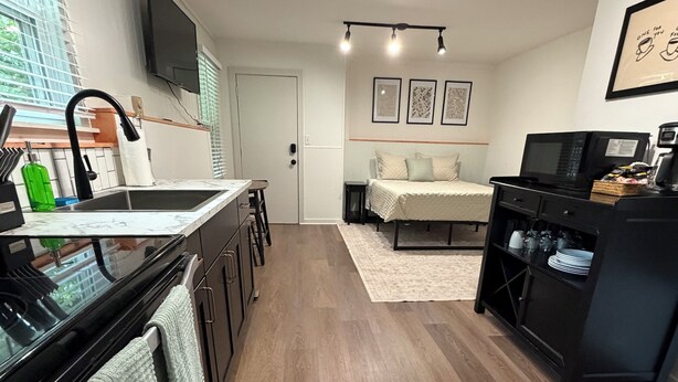 Een moderne keuken met een zwart aanrecht, een spoelbak en een fornuis. Er is een eethoek met een tafel en stoelen, en een slaapkamer met een bed en nachtkastje.