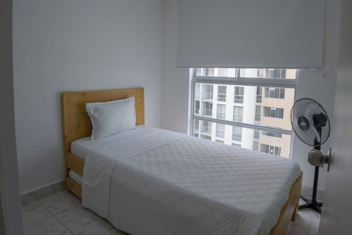 Un dormitorio con cama, ventilador, ventana y lámpara en el techo.