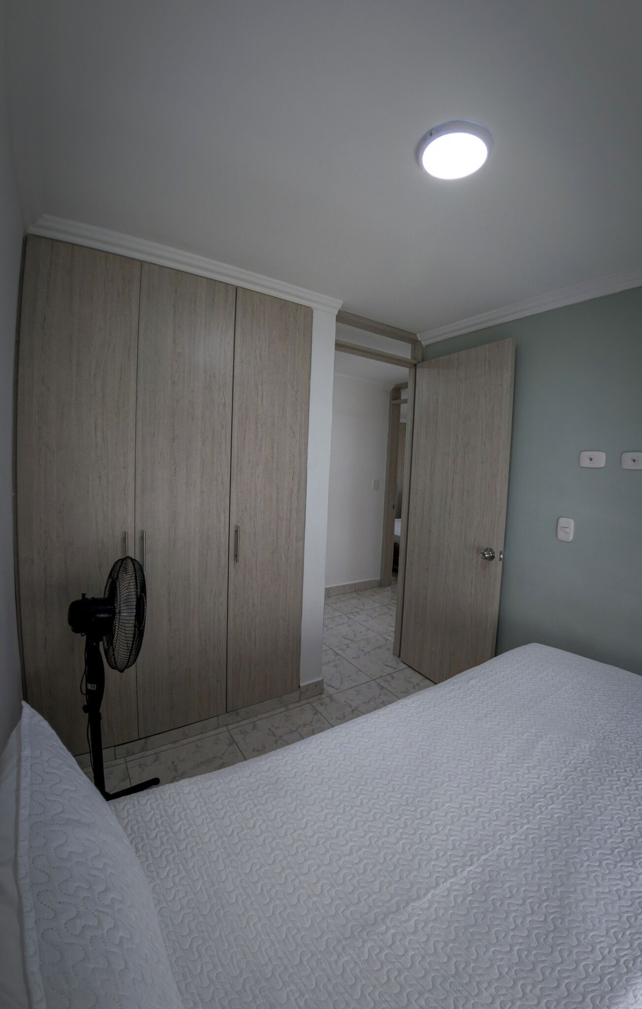 A bedroom with a bed, a standing fan, and a wardrobe.