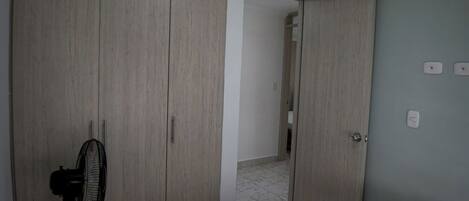 A bedroom with a bed, a standing fan, and a wardrobe.