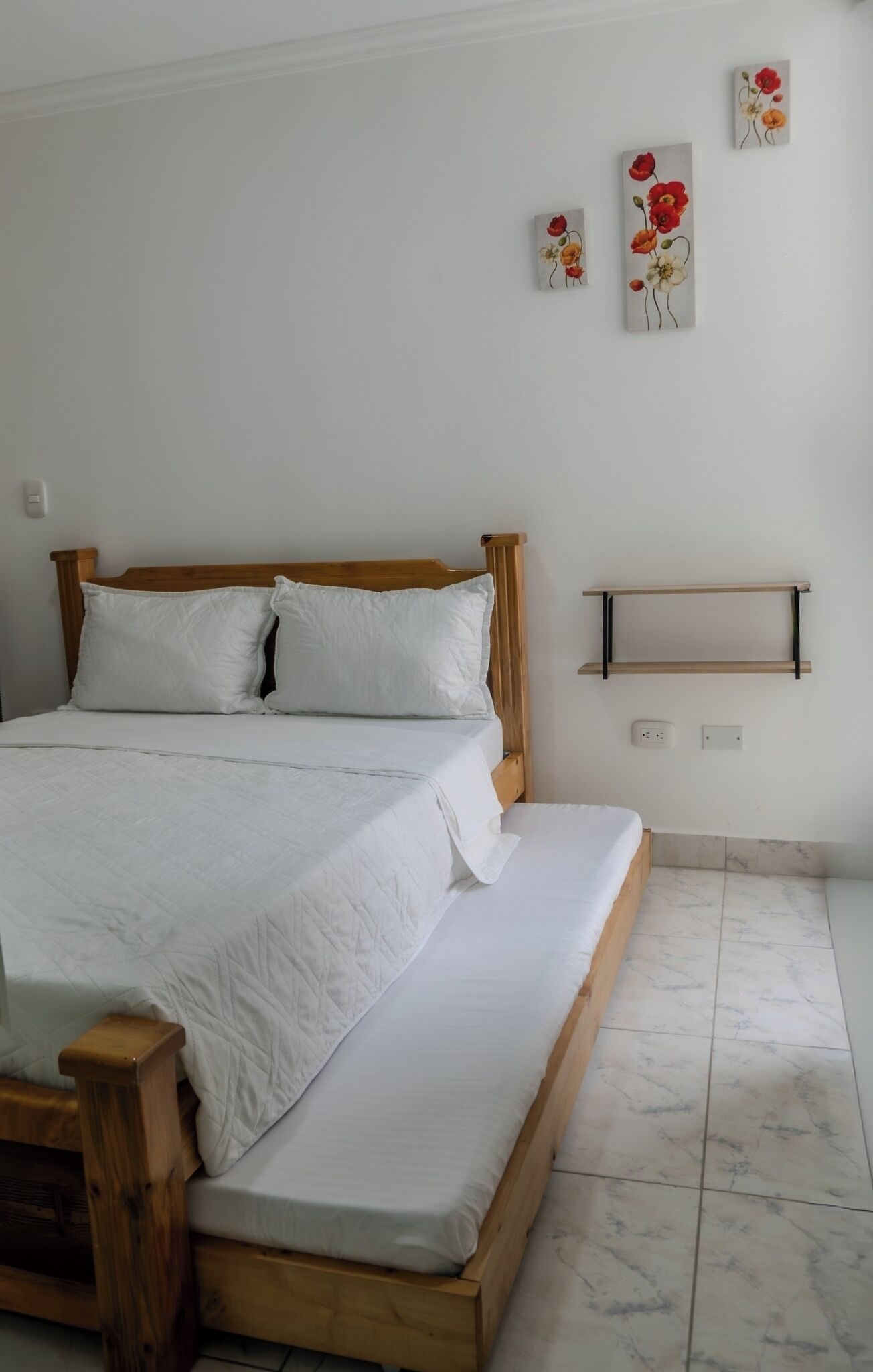 A bed with a wooden frame and white bedding, a wooden nightstand, and a wall-mounted shelf.