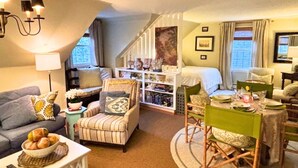 Ein gemütlicher Wohnbereich mit Sofa, Sessel, Esstisch und einer Treppe, die zu einem Schlafzimmer führt.