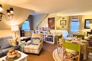 Ein gemütlicher Wohnbereich mit Sofa, Sessel, Esstisch und einer Treppe, die zu einem Schlafzimmer führt.