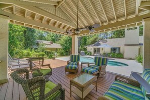 A covered outdoor area with wicker furniture, a pool, and a view of the surrounding greenery. - Sea Pines Escape with Private Pool (Hilton Head Island)