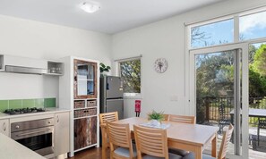 A compact kitchen with a gas stove, oven, and refrigerator, a dining table with chairs, and a view of the outdoors through a sliding glass door. - Phillip Island Resort Coastal Villa (Cowes)