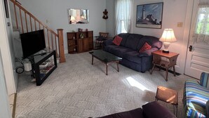 A living room with a television, sofa, coffee table, and a staircase.