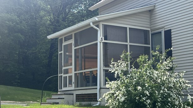 A house with a screened porch, a number '5' on the window, and a white flowering bush in the front yard.