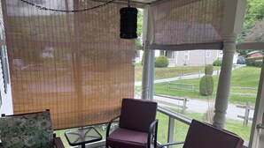 A covered porch with a table and two chairs, a hanging light fixture, and a view of a residential street.