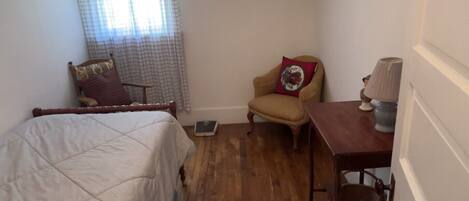 A small, cozy bedroom with a bed, a chair, a table, and a window with curtains.