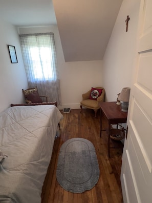 Un dormitorio pequeño y acogedor con cama, una silla, una mesa y una ventana con cortinas.
