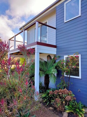 A two-story house with a balcony, surrounded by various plants and shrubs. - Comfortable  Peaceful Island Holiday Getaway (Rhyll)
