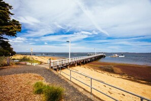 A coastal walkway leading to a pier with a sandy beach and a calm sea in the background. - Comfortable  Peaceful Island Holiday Getaway (Rhyll)