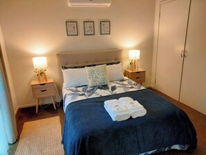 A neatly made bed with a floral-patterned duvet, two bedside lamps, a small bedside table with a plant, and a wardrobe. - Comfortable  Peaceful Island Holiday Getaway (Rhyll)