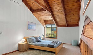 A bedroom with a wooden ceiling, a bed, a nightstand, a lamp, a window, and a painting on the wall. - Seashell - Minutes walk to Beach. Phillip Island (Cape Woolamai)
