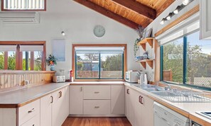 A kitchen with wooden cabinets, a built-in oven, a sink, and a window with a view of the outdoors. - Seashell - Minutes walk to Beach. Phillip Island (Cape Woolamai)