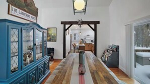 Ein Essbereich mit einem langen Holztisch, einem blauen Schrank mit Glastüren und Blick in die Küche durch einen offenen Durchgang.